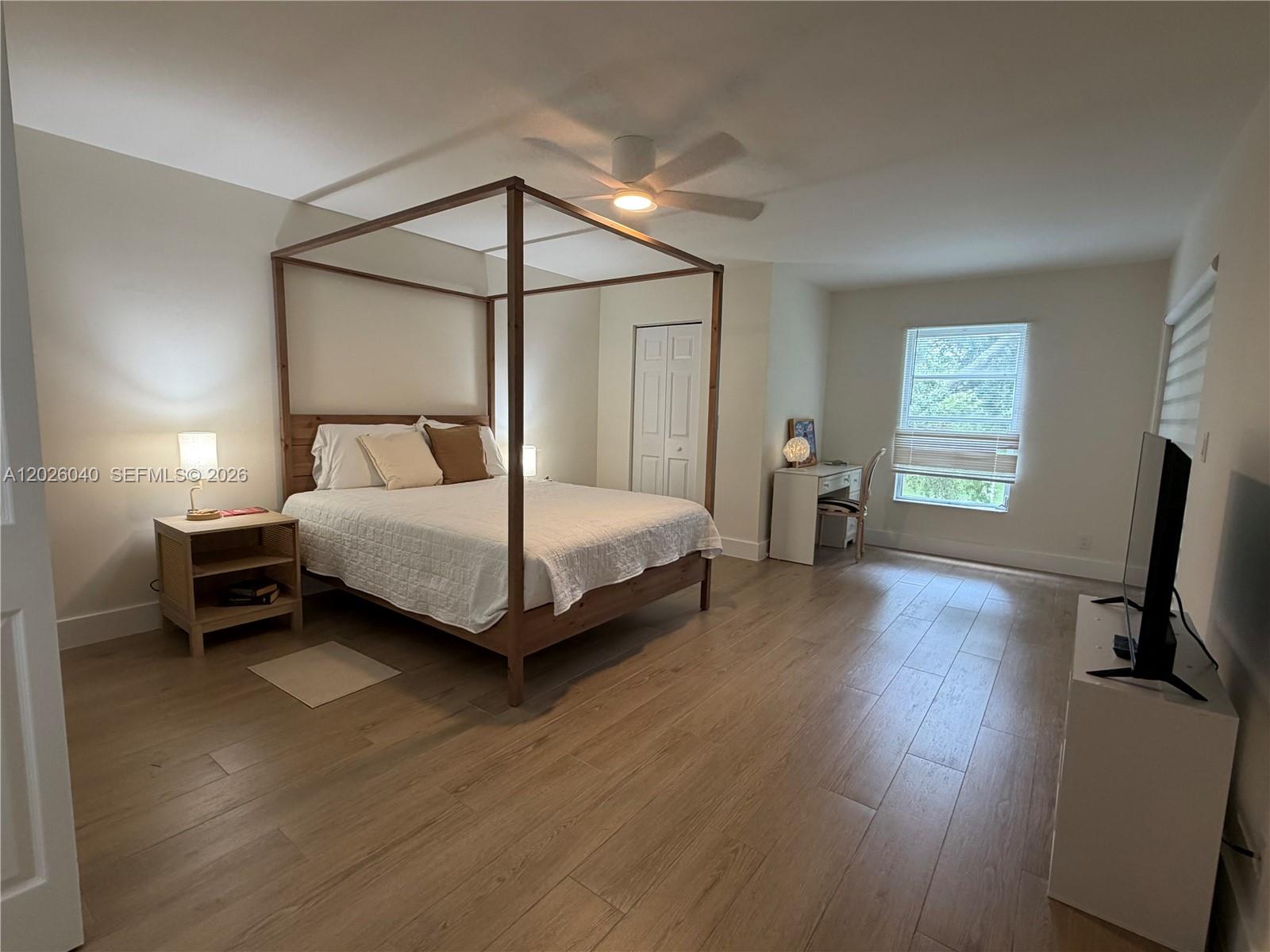 A bedroom features a wooden canopy bed, light wood-look flooring, and a small desk area — 7350 Kinghurst Dr # 305, Delray Beach FL 33446, DELRAY BEACH, FL