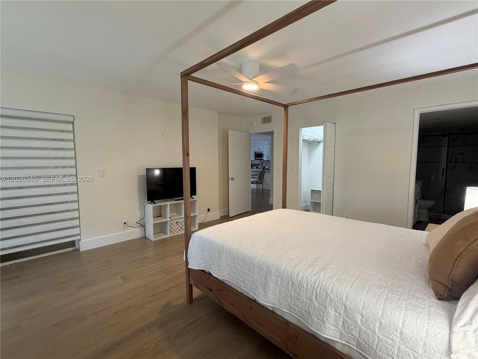 A bedroom features a wooden canopy bed, light wood flooring, and a white walk-in closet — 7350 Kinghurst Dr # 305, Delray Beach FL 33446, DELRAY BEACH, FL