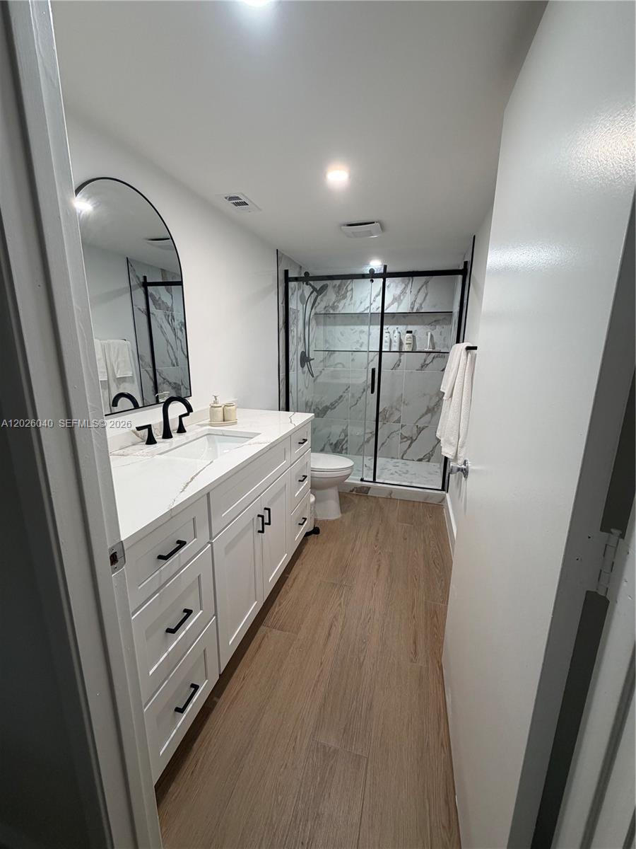 A bathroom features a white vanity with black hardware, a marble-look shower, and wood-look flooring — 7350 Kinghurst Dr # 305, Delray Beach FL 33446, DELRAY BEACH, FL