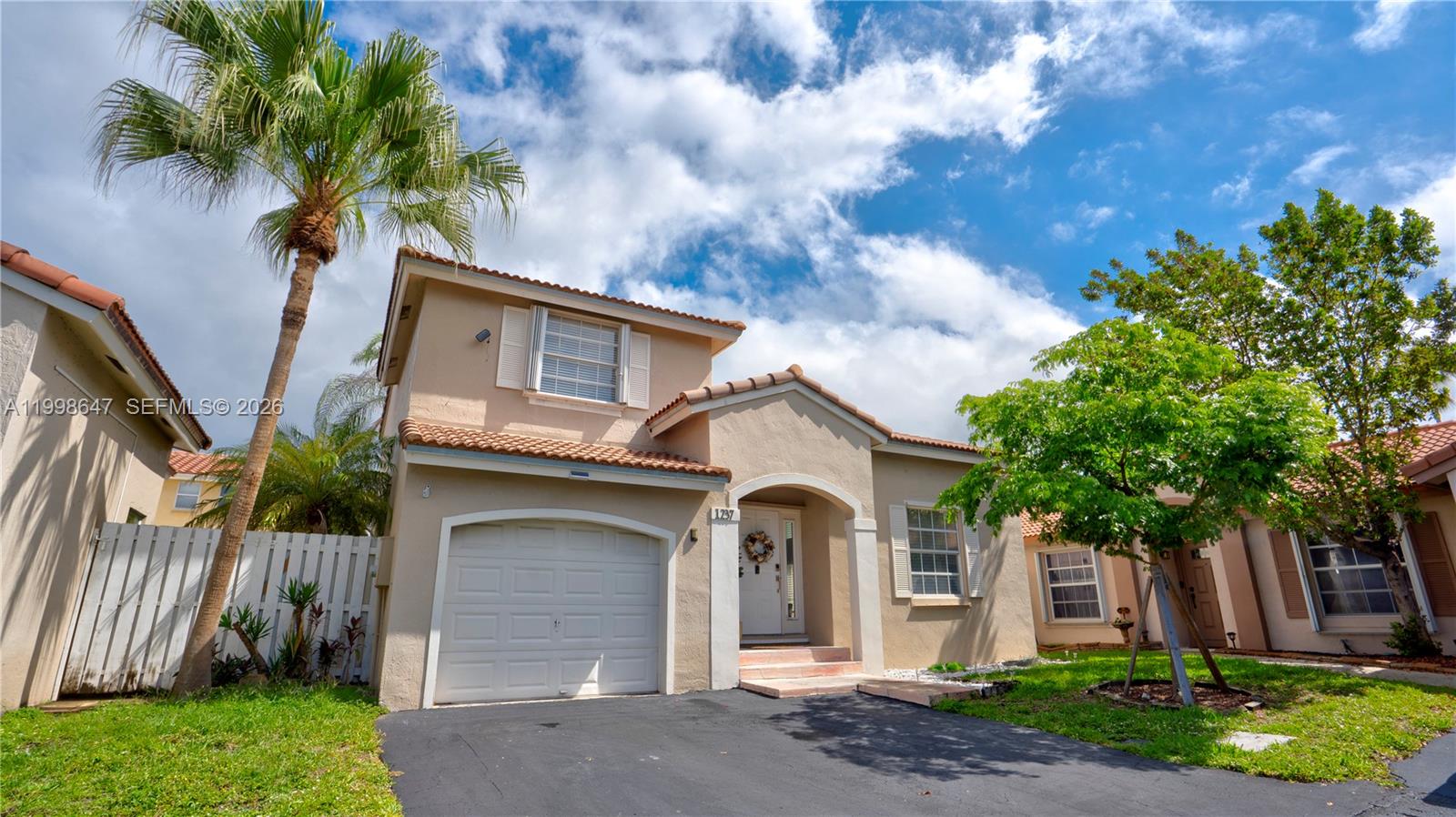 A two-story tan stucco house features a single-car garage, a palm tree, and a driveway — 1237 NW 125th Ter, Sunrise FL 33323, SUNRISE, FL