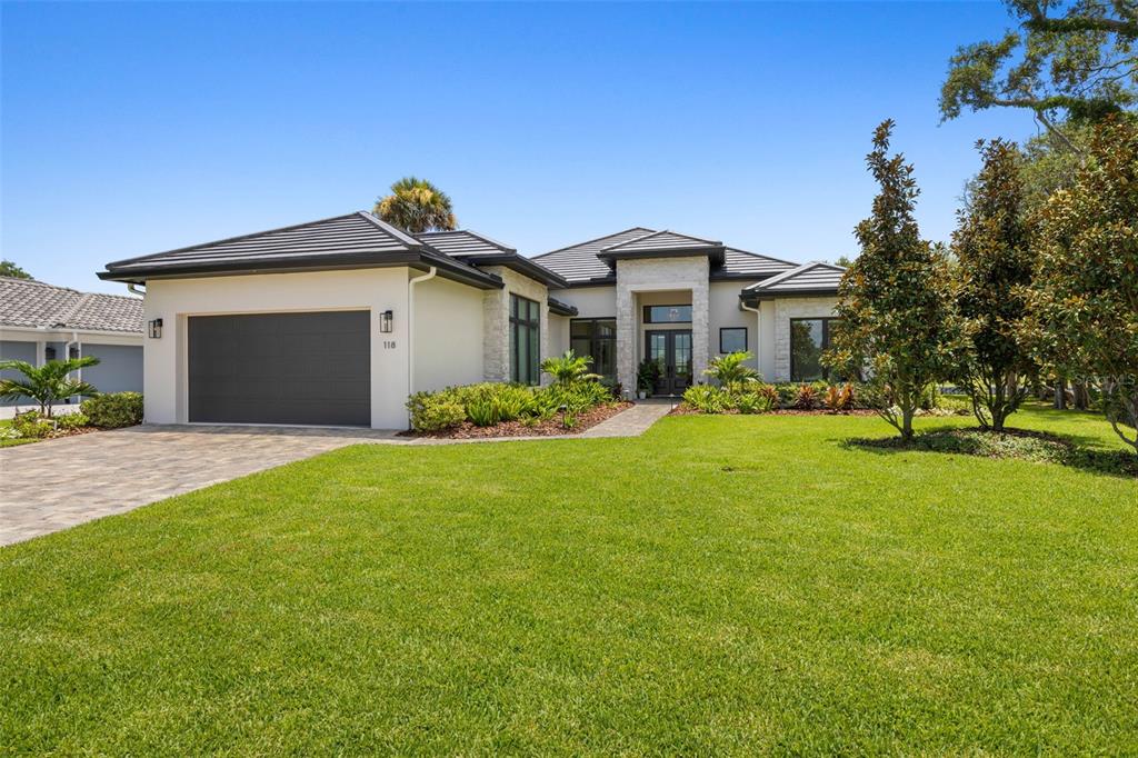 A modern single-story house with a dark garage door, stone accents, and a landscaped lawn — 118 SEASIDE LANDINGS DRIVE N, FLAGLER BEACH, FL