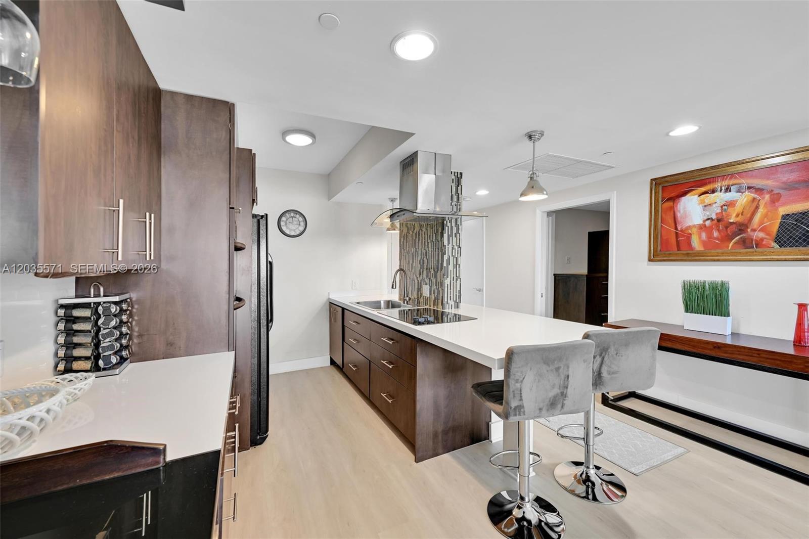 A modern kitchen features dark wood cabinets, white countertops, a breakfast bar, and stainless appliances — 1850 S Ocean Dr # 1907, Hallandale Beach FL 33009, HALLANDALE BEACH, FL