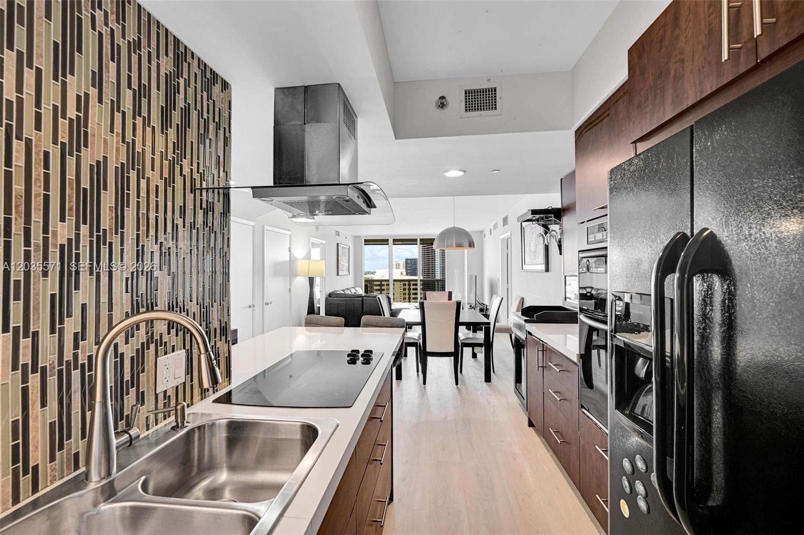A modern kitchen features dark wood cabinets, a glass-tiled backsplash, and a stainless steel range hood — 1850 S Ocean Dr # 1907, Hallandale Beach FL 33009, HALLANDALE BEACH, FL