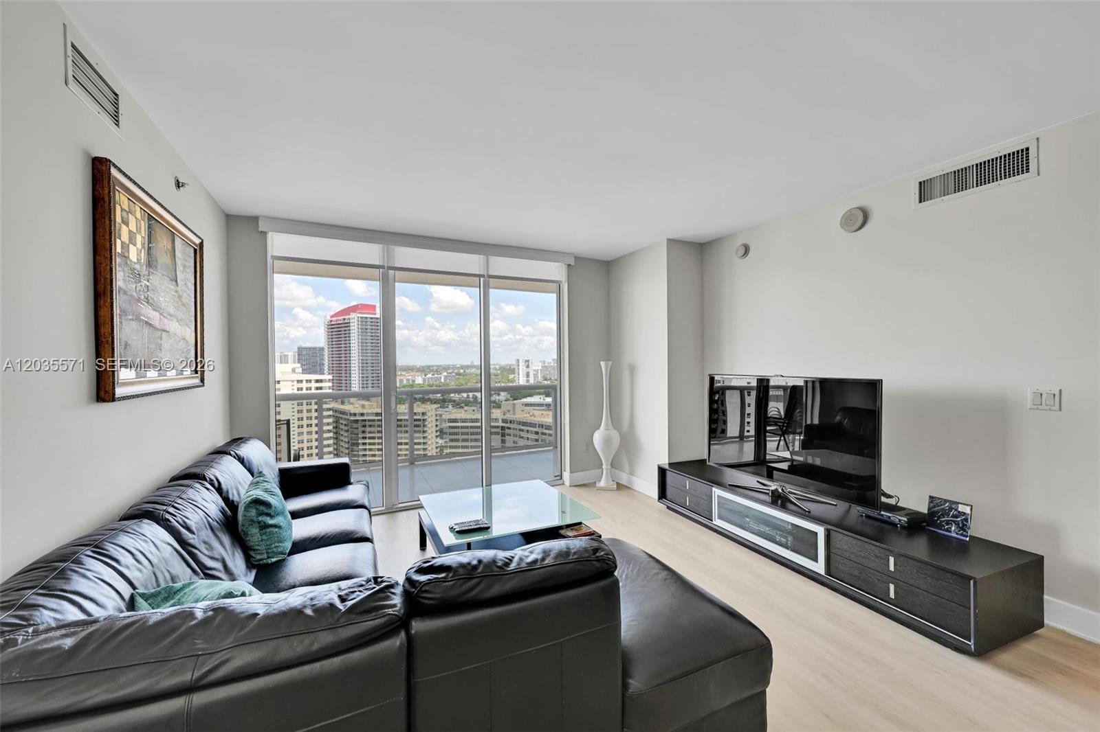 A living room features a black leather sectional, glass coffee table, and city skyline views — 1850 S Ocean Dr # 1907, Hallandale Beach FL 33009, HALLANDALE BEACH, FL