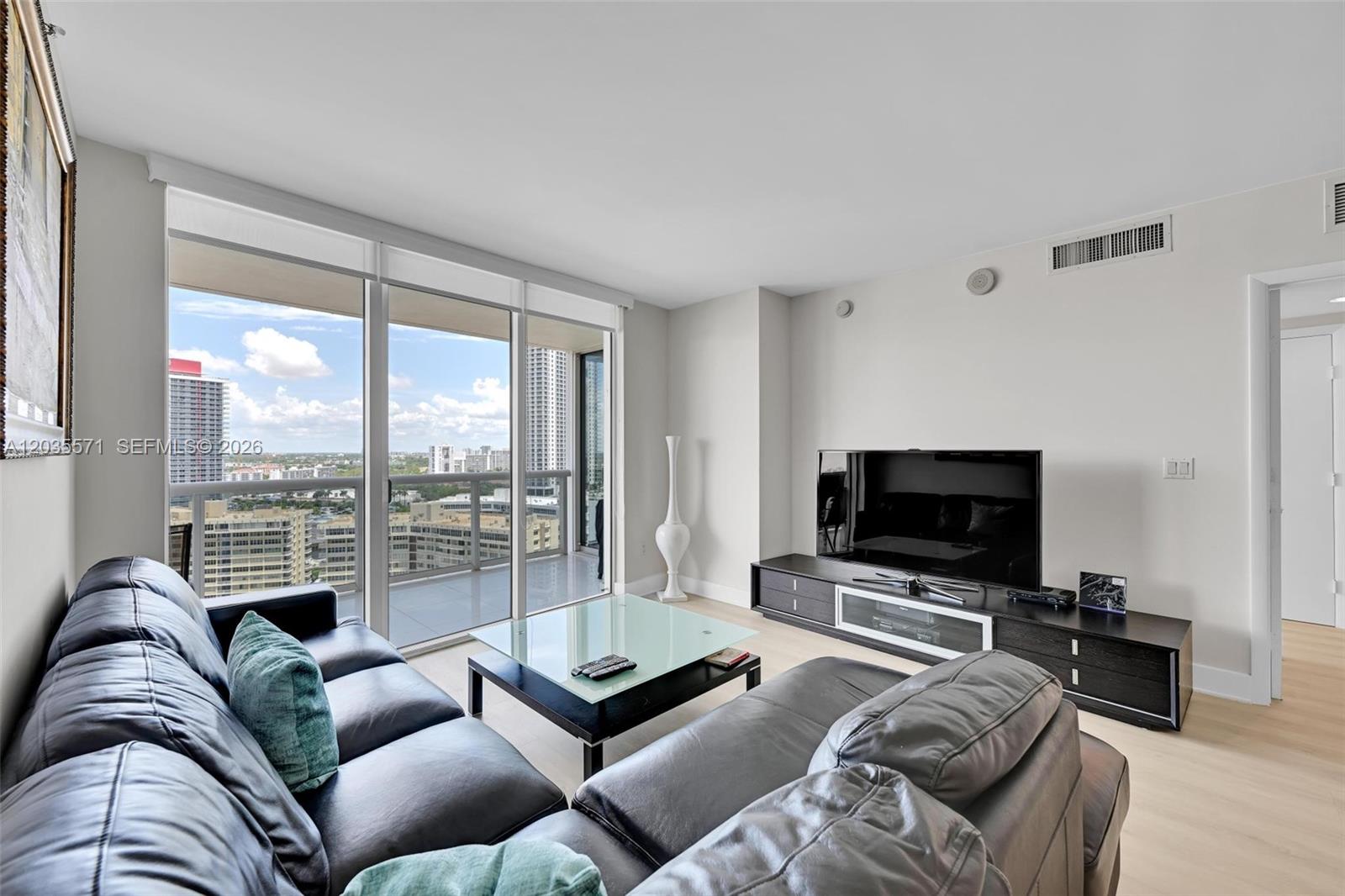 A living room features a black leather sofa, glass coffee table, and a city view balcony — 1850 S Ocean Dr # 1907, Hallandale Beach FL 33009, HALLANDALE BEACH, FL
