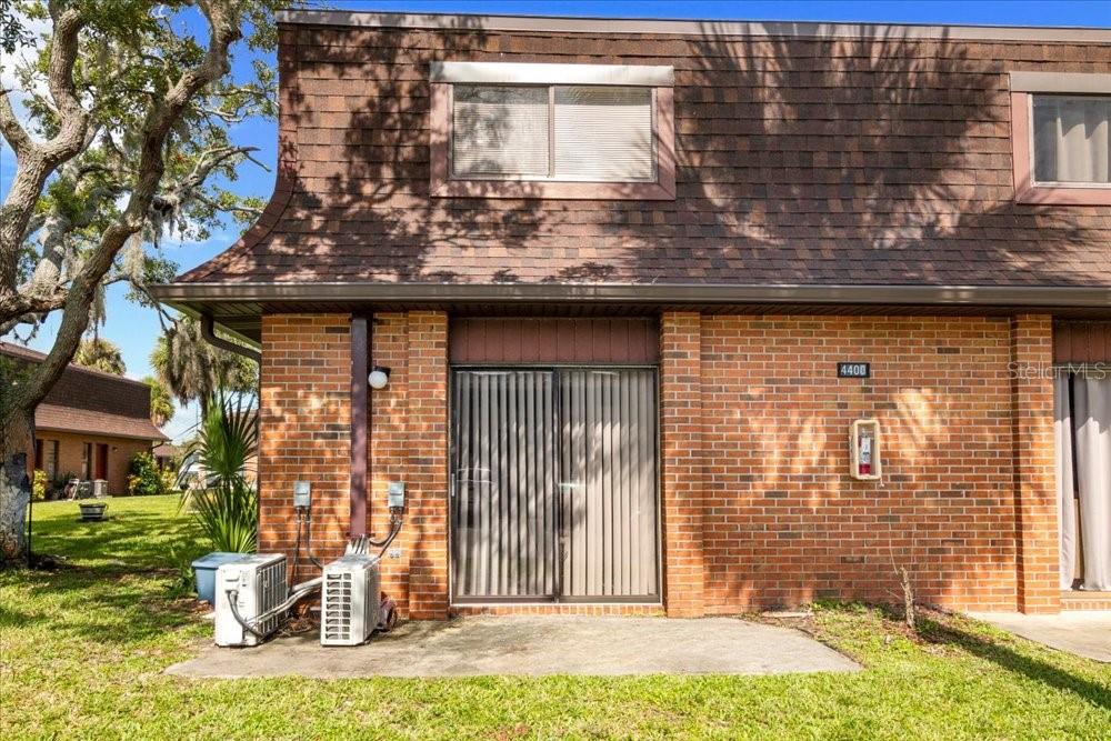 A brick townhouse exterior features a sliding glass door, two air conditioning units, and windows — 4414 OVERLOOK DRIVE NE UNIT 18, PALM BAY, FL