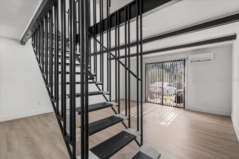 A room with light wood-look flooring features a black metal staircase and sliding glass doors — 4414 OVERLOOK DRIVE NE UNIT 18, PALM BAY, FL