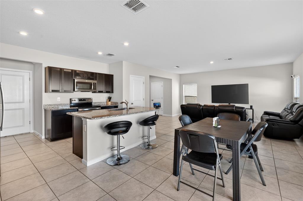 An open-concept kitchen and living area features dark cabinetry, granite countertops, and tile flooring — 5007 STARBOARD STREET, HAINES CITY, FL