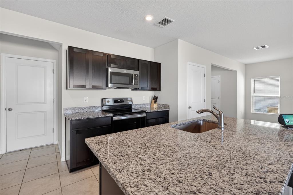 A kitchen features dark wood cabinets, granite countertops, a center island, and stainless steel appliances — 5007 STARBOARD STREET, HAINES CITY, FL