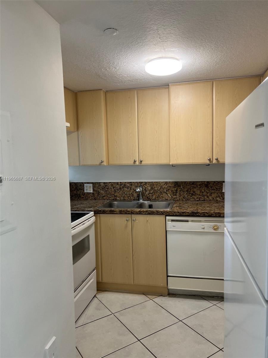 A kitchen features light wood cabinets, granite countertops, white appliances, and tiled flooring — 12645 SW 91st St # 202, Miami FL 33186, MIAMI, FL