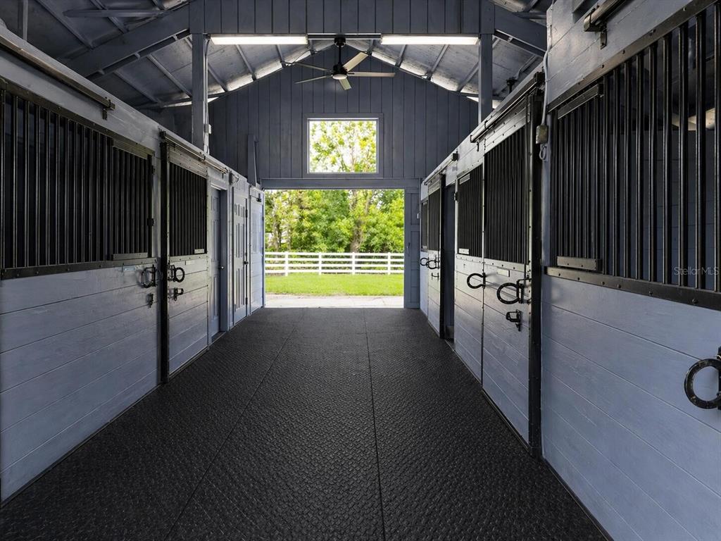 A view down the center aisle of a horse barn with blue stalls and flooring — 33015 SAHARA COURT, SORRENTO, FL