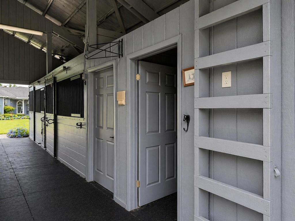 A gray-painted stable aisle features multiple stall doors, a ladder-style wall rack, and electrical outlets — 33015 SAHARA COURT, SORRENTO, FL