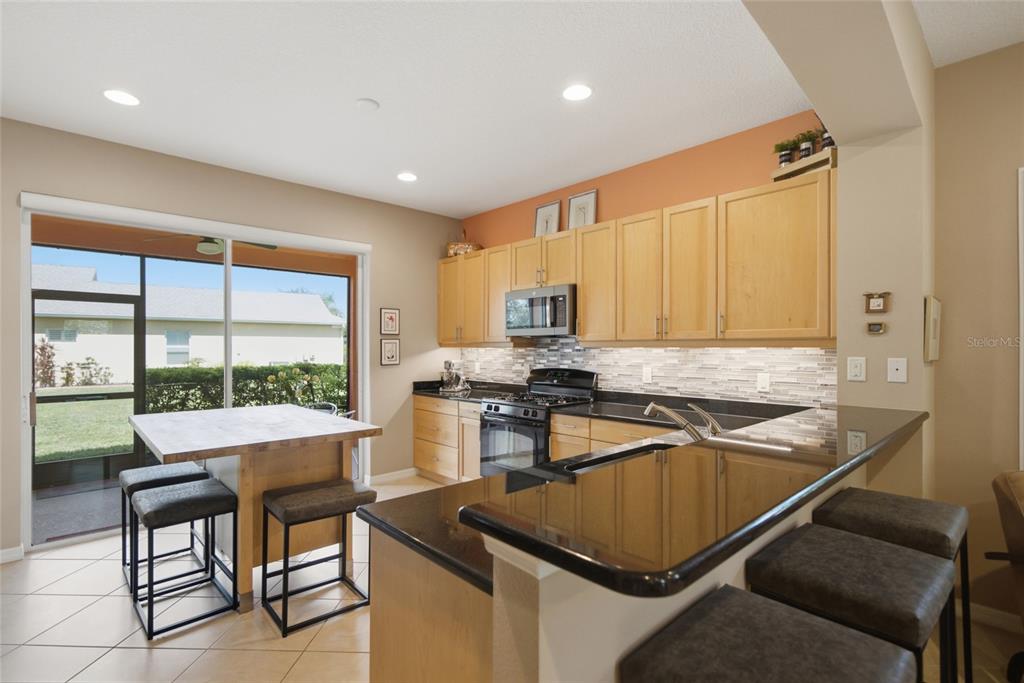 A kitchen features light wood cabinets, black countertops, a center island, and a sliding glass door — 5002 BOSTON COMMON GLEN, BRADENTON, FL