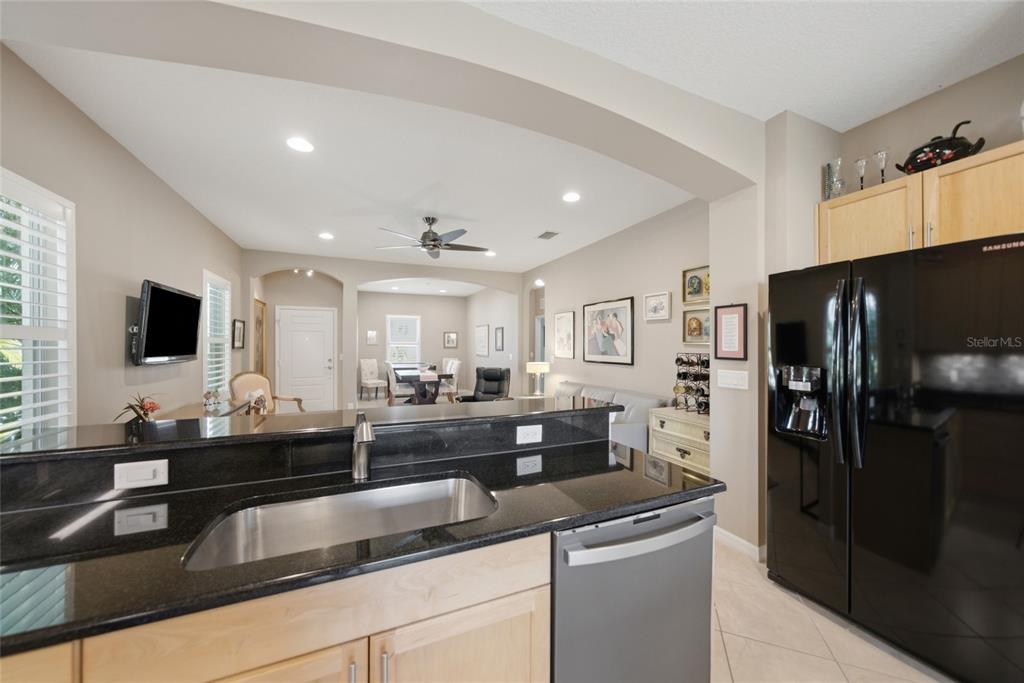 A kitchen with black granite countertops and a stainless steel sink overlooks a living area — 5002 BOSTON COMMON GLEN, BRADENTON, FL