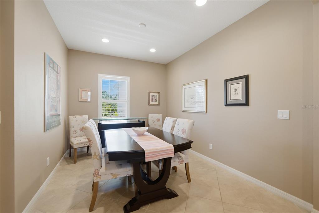 A dining room features a dark wood table, upholstered chairs, beige walls, and tile flooring — 5002 BOSTON COMMON GLEN, BRADENTON, FL