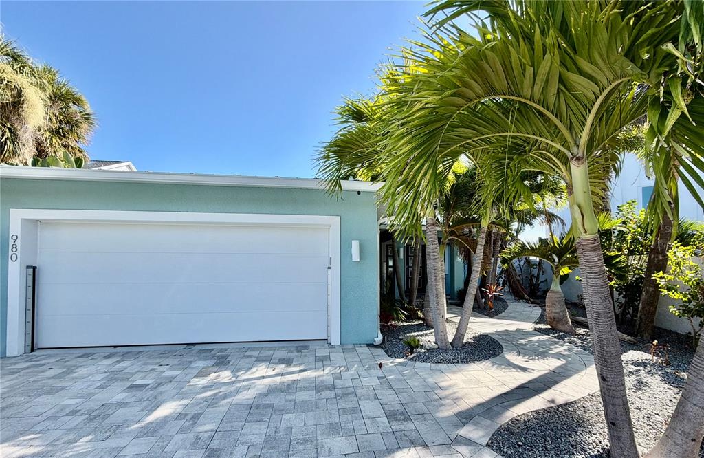 A light blue house exterior features a white garage door, palm trees, and stone pavers — 980 BOCA CIEGA ISLE DRIVE, ST PETE BEACH, FL