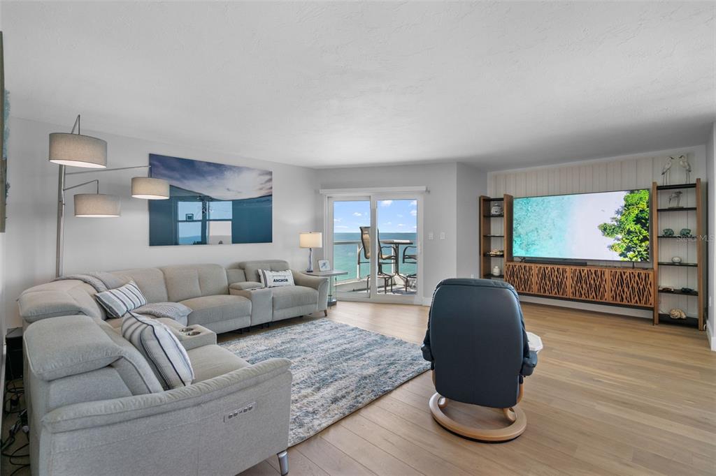 A living room features a sectional sofa, a blue armchair, and a large television with ocean views — 1050 LONGBOAT CLUB ROAD UNIT 901, LONGBOAT KEY, FL
