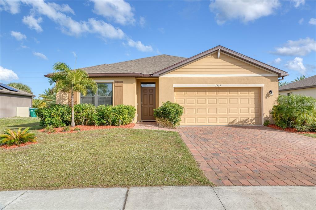 A single-story house with a tan stucco exterior, a two-car garage, and a brick driveway — 7339 TOURMALINE DRIVE, GRANT VALKARIA, FL