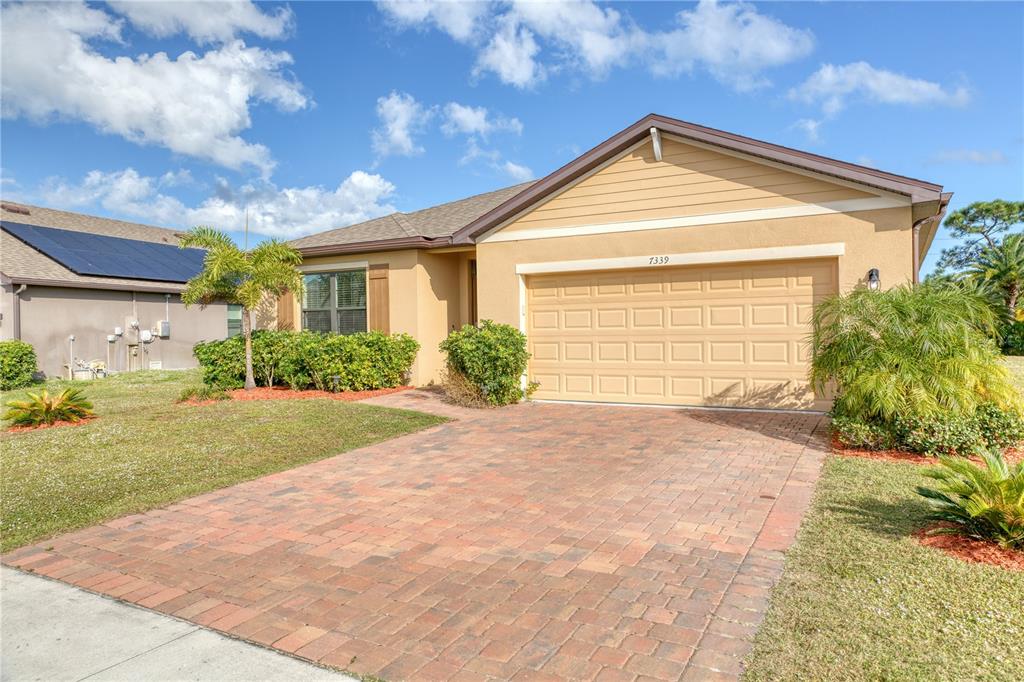 A single-story house with a tan stucco exterior, a brick paver driveway, and a garage — 7339 TOURMALINE DRIVE, GRANT VALKARIA, FL