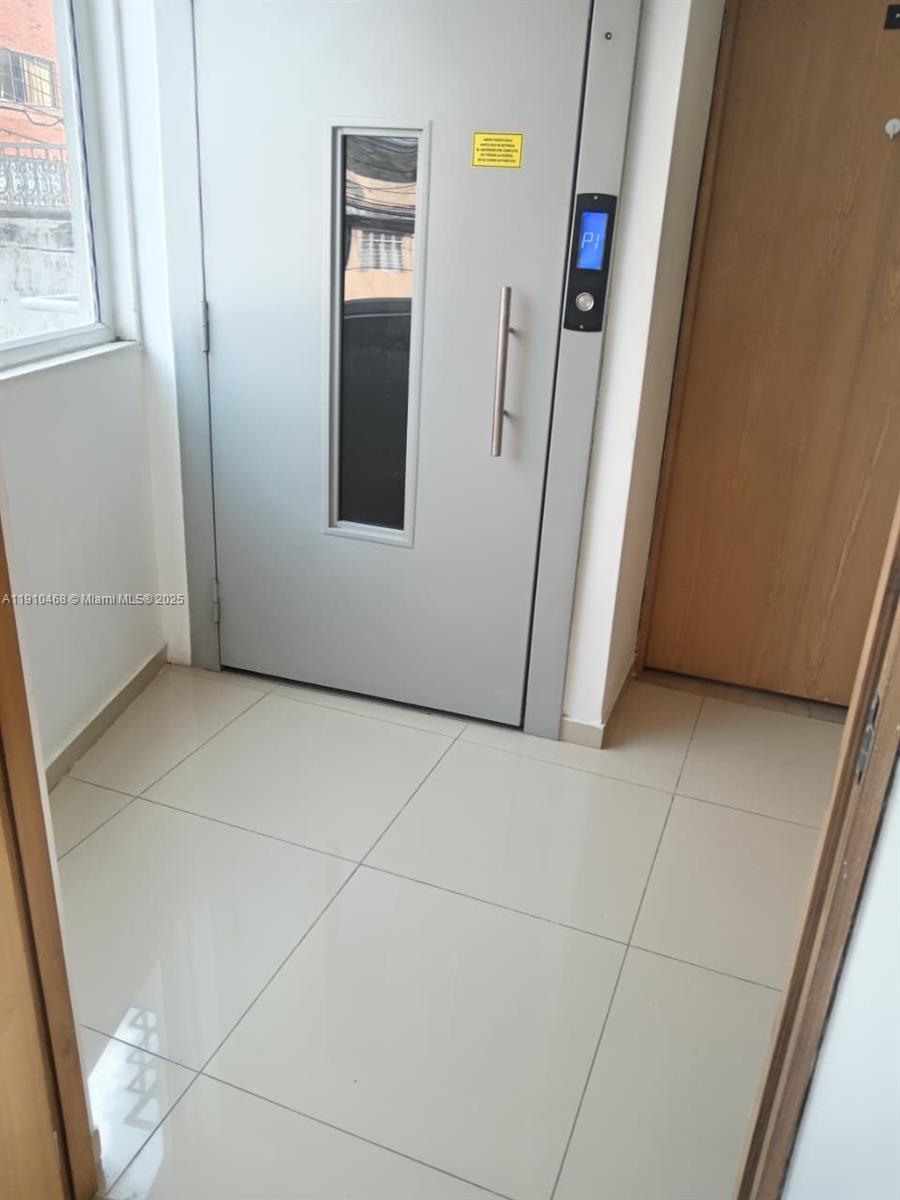 A tiled hallway features a gray elevator door with a vertical window and handle — Calle 2 Oeste #24A174 Miraflor # 101, 00000, FL