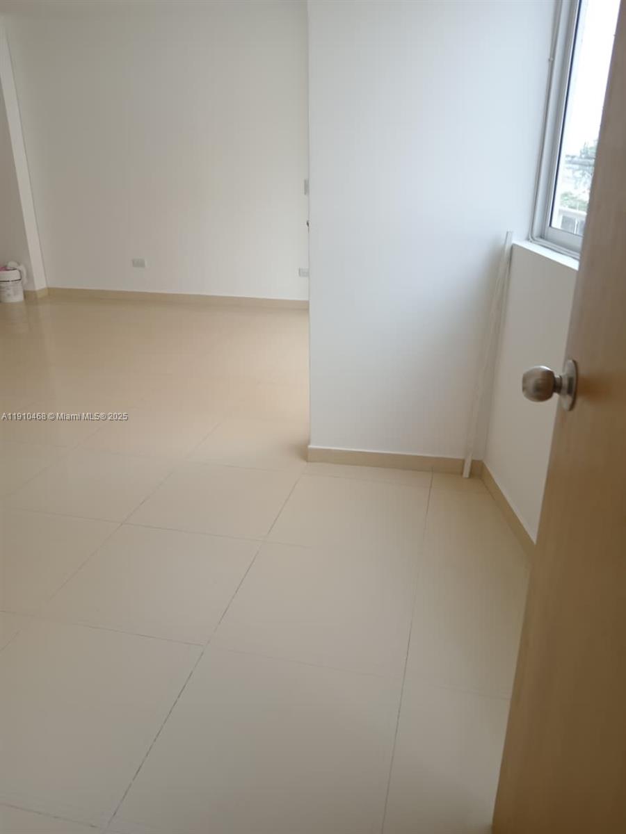 An empty room features light-colored tile flooring, white walls, and a window — Calle 2 Oeste #24A174 Miraflor # 101, 00000, FL