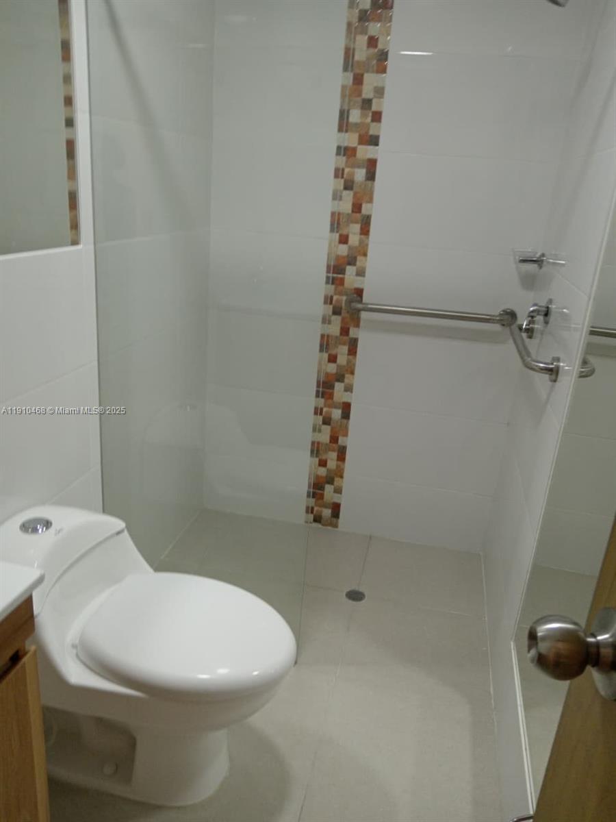 A bathroom features a white toilet, a walk-in shower with a grab bar, and tiled walls — Calle 2 Oeste #24A174 Miraflor # 101, 00000, FL