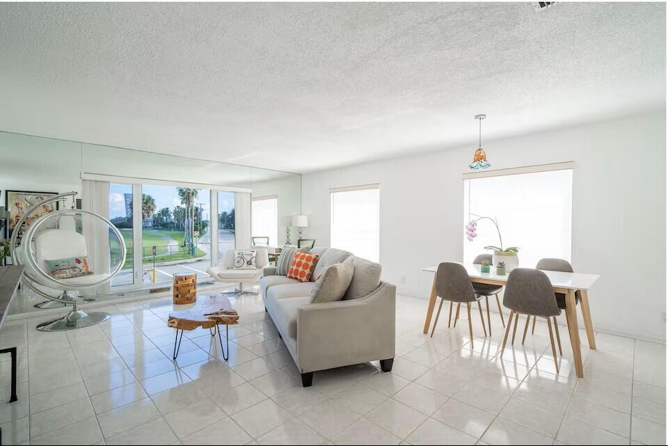 A bright living and dining area features white tile floors, a mirrored wall, and furniture — 6 Lucerne Avenue # 3, FL 33460, FL