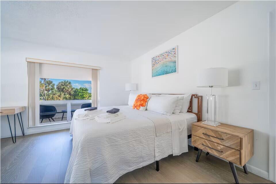 A bedroom features a bed with white bedding, a wooden nightstand, and a balcony view — 6 Lucerne Avenue # 3, FL 33460, FL
