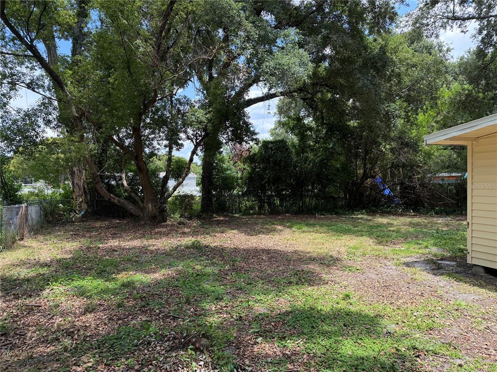 A grassy backyard features large mature trees and a chain-link fence along the perimeter — 1496 33RD STREET NW, WINTER HAVEN, FL