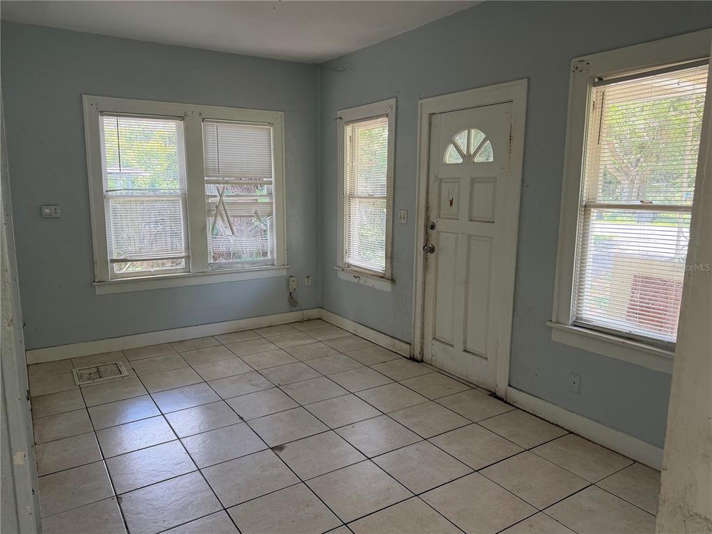 An empty room with light blue walls, tile flooring, multiple windows, and a white door — 1496 33RD STREET NW, WINTER HAVEN, FL