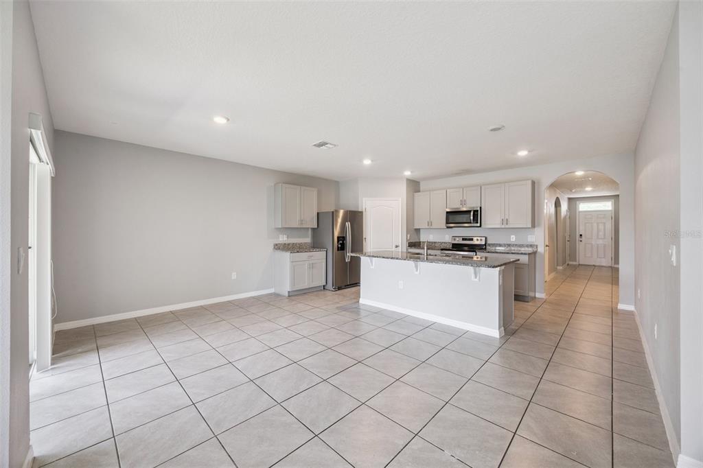 An open-concept kitchen and dining area features gray cabinetry, granite countertops, and tile flooring — 1603 BARBERRY DRIVE, KISSIMMEE, FL