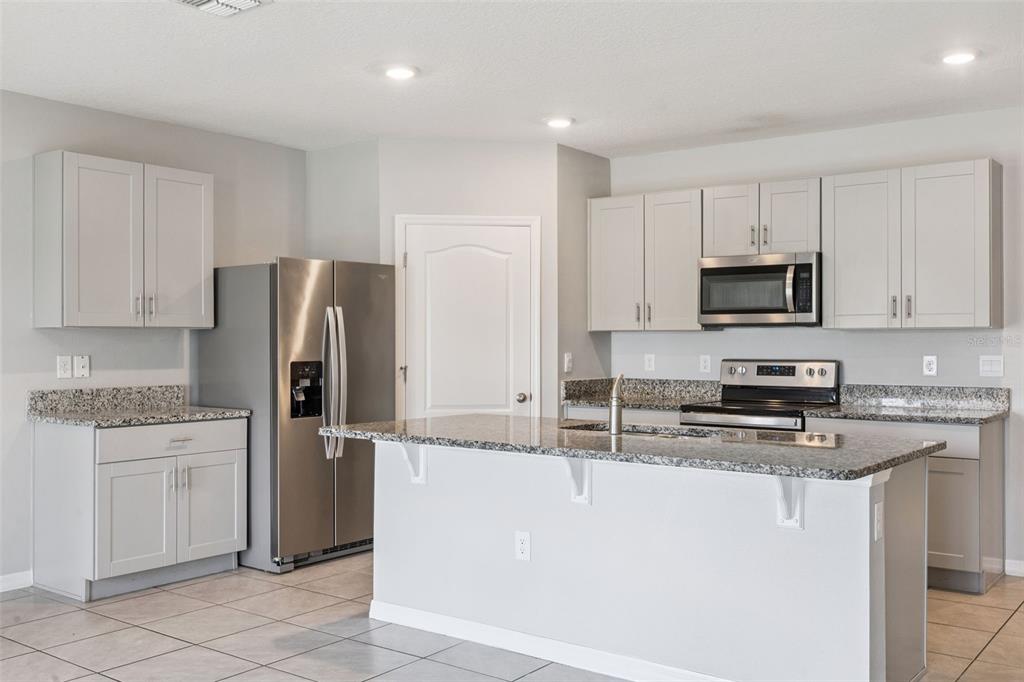 A kitchen with light gray cabinets, granite countertops, stainless steel appliances, and a central island — 1603 BARBERRY DRIVE, KISSIMMEE, FL