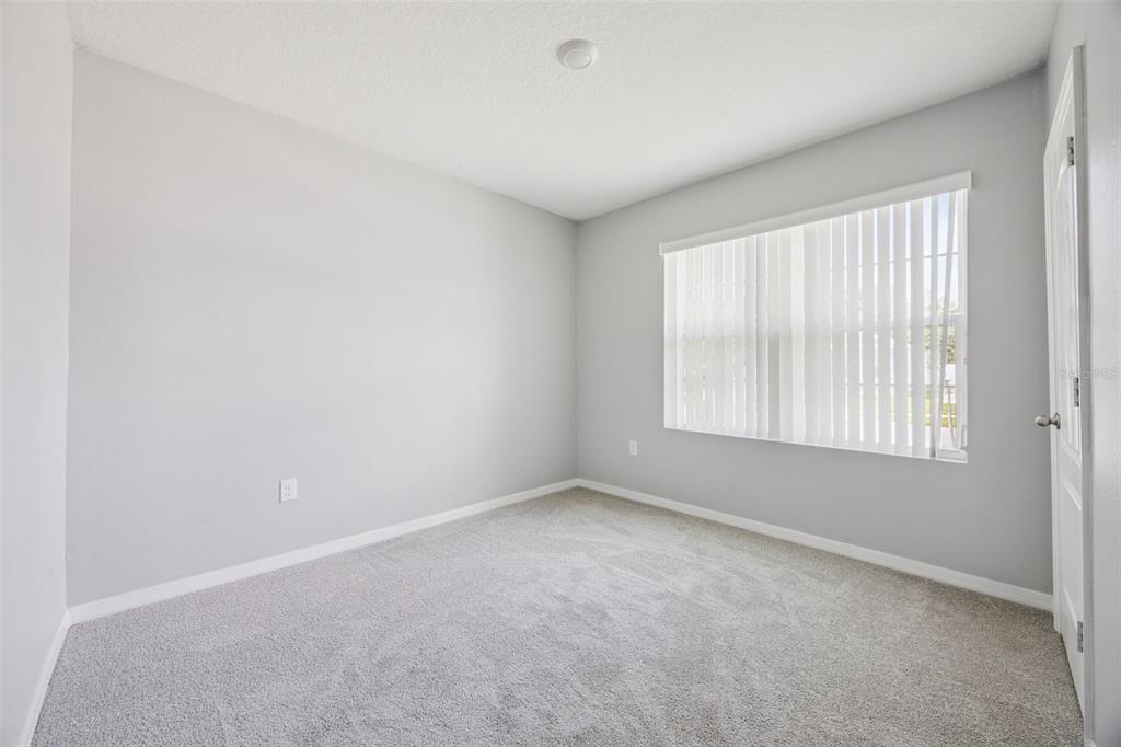 An empty bedroom features light gray walls, beige carpeting, and a window with vertical blinds — 1603 BARBERRY DRIVE, KISSIMMEE, FL