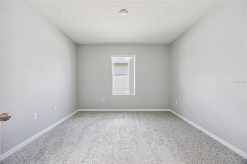 An empty bedroom features light gray walls, beige carpeting, and a single centered window — 1603 BARBERRY DRIVE, KISSIMMEE, FL