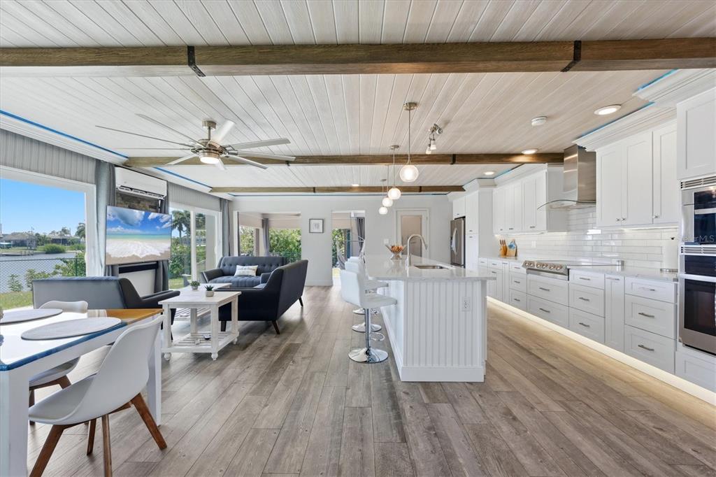 An open-concept kitchen and living area features white cabinetry, wood-look flooring, and exposed ceiling beams — 108 BUCKEYE AVENUE NW, PORT CHARLOTTE, FL
