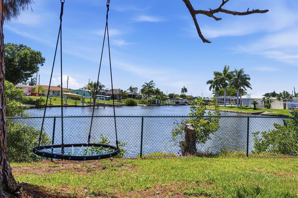 A round web swing hangs in a grassy yard overlooking a canal with waterfront homes — 108 BUCKEYE AVENUE NW, PORT CHARLOTTE, FL