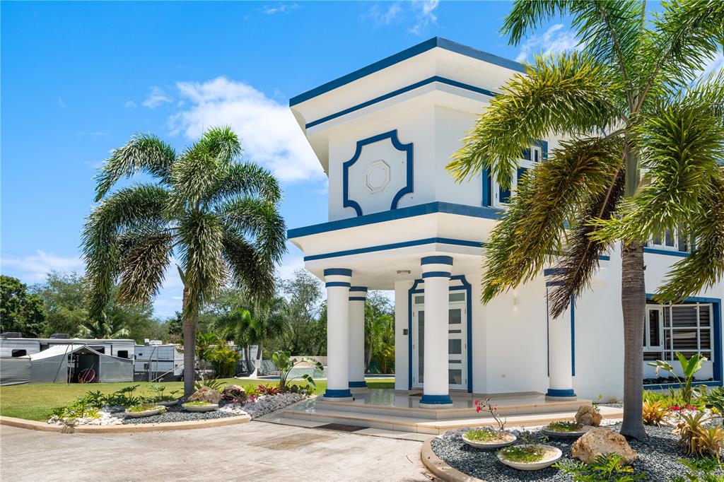 A white two-story house with blue trim and columns stands near palm trees — 1 CALLE ISAMAR, ISABELA, PR
