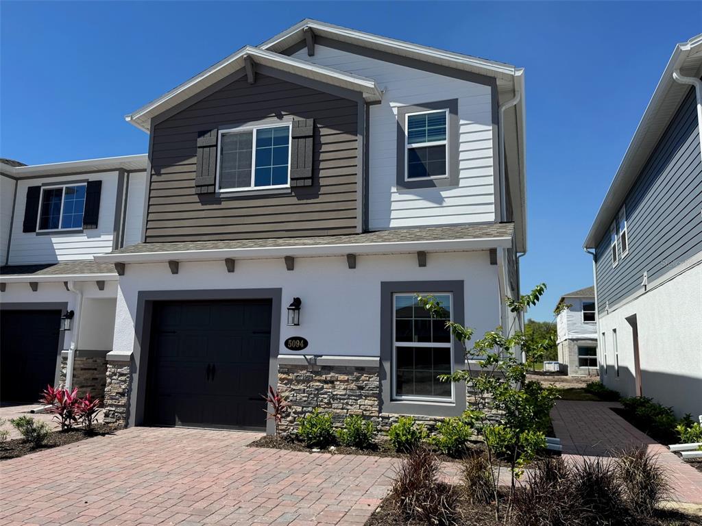 A two-story townhouse with a stone-accented facade, a single-car garage, and a brick paver driveway — 5094 RAIN SHADOW DRIVE, ST CLOUD, FL