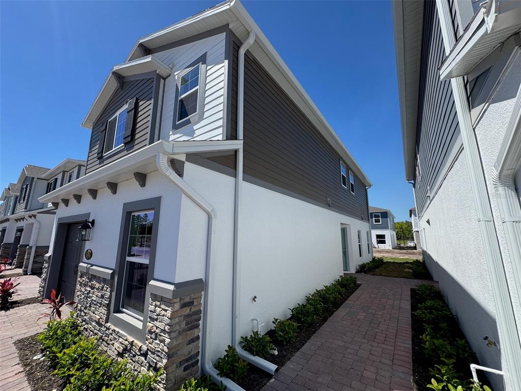 A side view of a two-story house with white stucco, gray siding, and stone accents — 5094 RAIN SHADOW DRIVE, ST CLOUD, FL