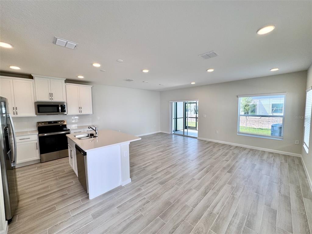 An open-concept kitchen and living area features white cabinetry, stainless appliances, and light wood-look flooring — 5094 RAIN SHADOW DRIVE, ST CLOUD, FL