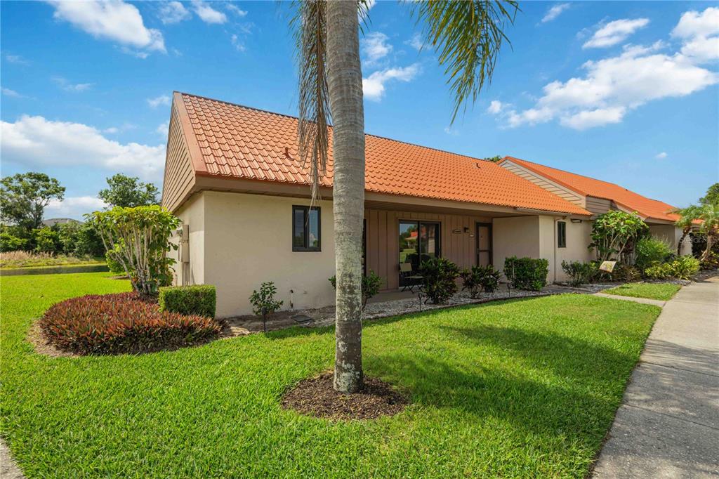 A single-story villa with a terracotta tile roof and a palm tree in the yard — 6567 DRAW LANE UNIT 104, SARASOTA, FL