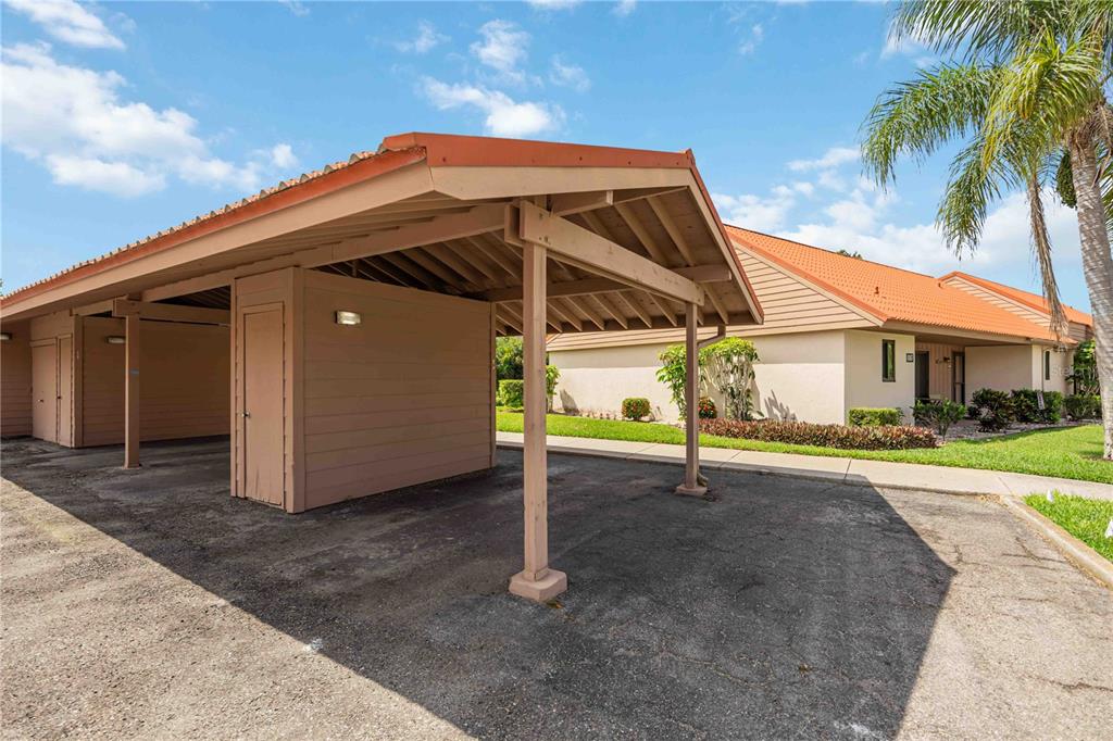 A covered carport with a storage unit stands in front of a single-story residential building — 6567 DRAW LANE UNIT 104, SARASOTA, FL