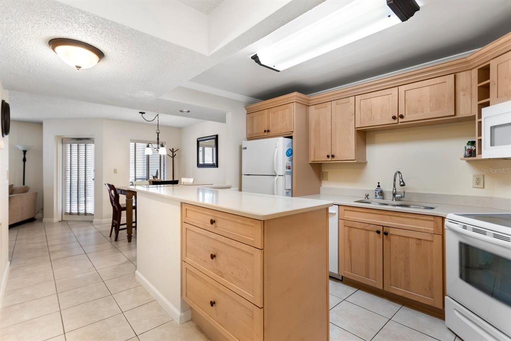A kitchen with light wood cabinets, white appliances, and a breakfast bar overlooks a dining area — 1515 PINELLAS BAYWAY UNIT C31, TIERRA VERDE, FL