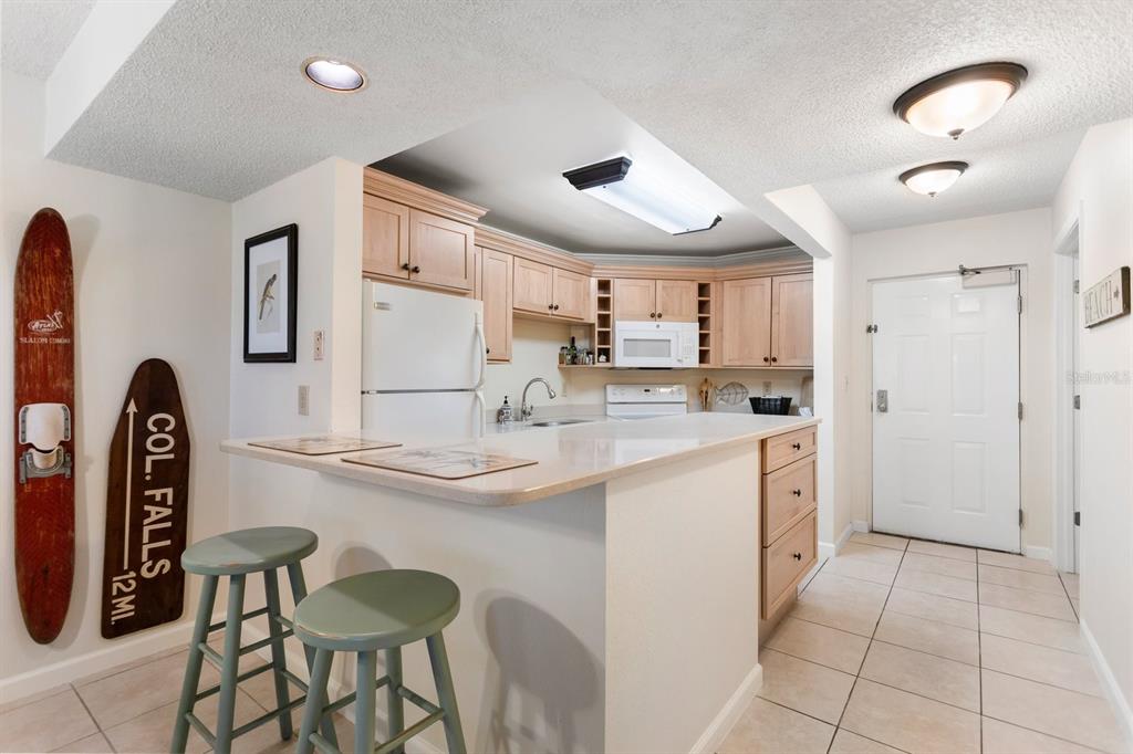 A kitchen features light wood cabinets, a white refrigerator, a breakfast bar, and tiled floors — 1515 PINELLAS BAYWAY UNIT C31, TIERRA VERDE, FL
