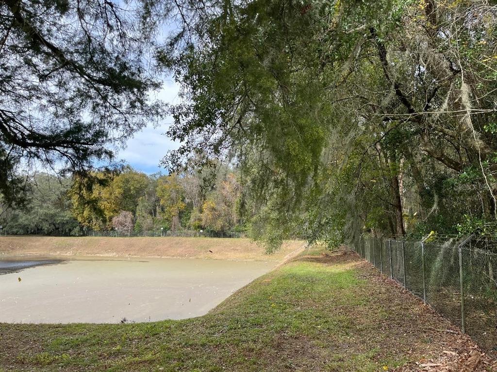 A fenced retention pond sits beside a grassy bank lined with mature, moss-draped trees — 1602A SW WILLISTON ROAD, GAINESVILLE, FL