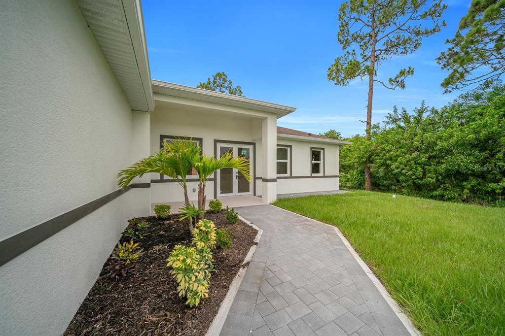 A paved walkway leads to the front entrance of a house with a small palm tree — 2715 10TH STREET W, LEHIGH ACRES, FL