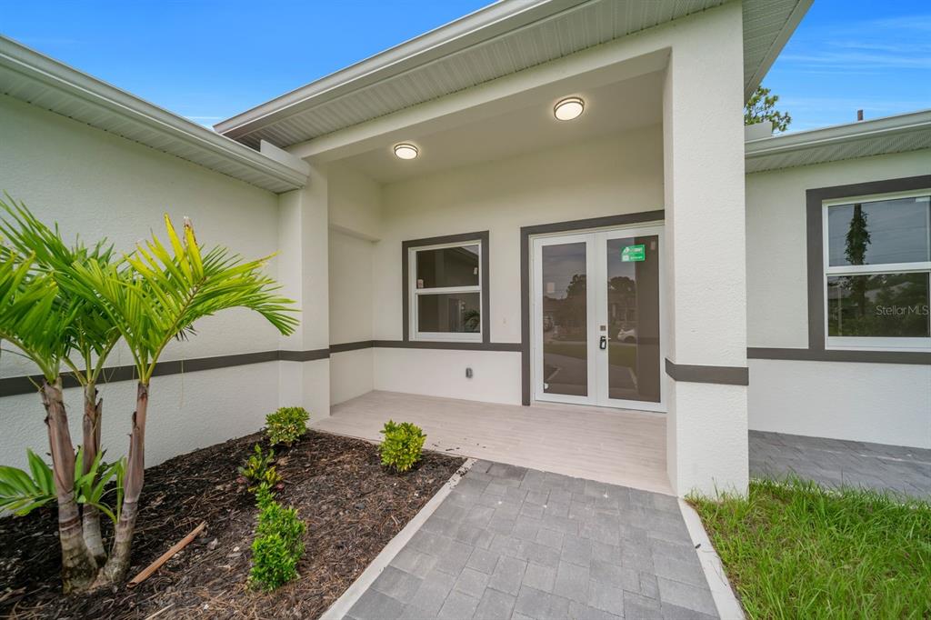 A covered entryway with a paver walkway, a palm tree, and double glass front doors — 2715 10TH STREET W, LEHIGH ACRES, FL
