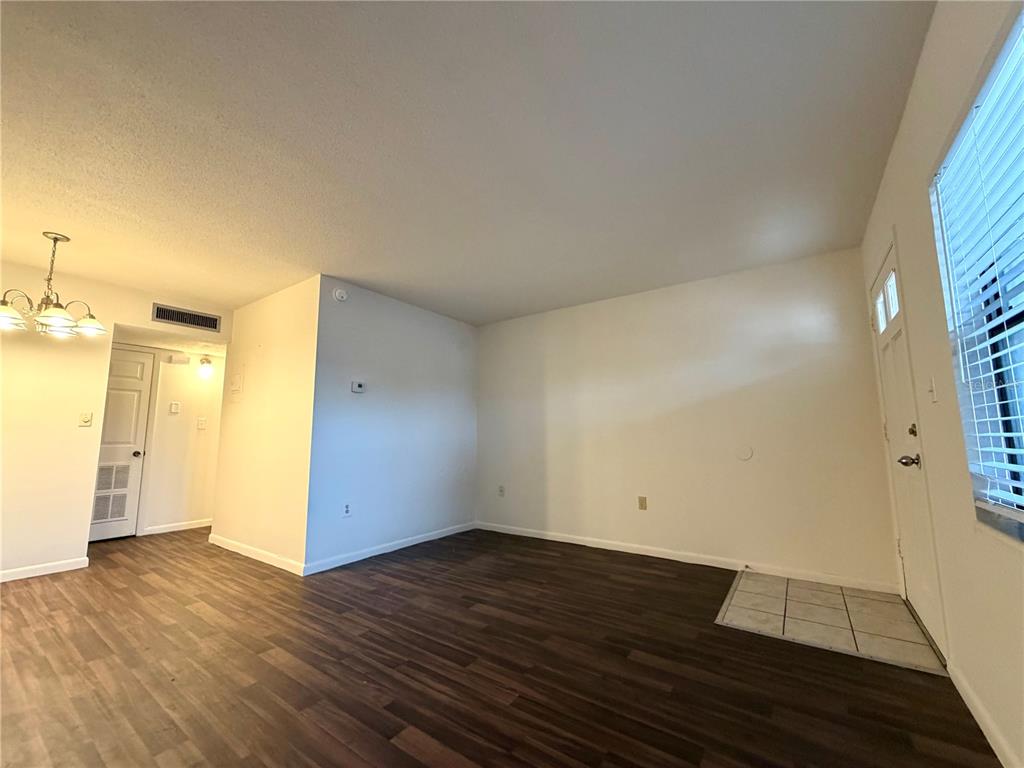 An empty living room features dark wood-look flooring, white walls, and a tiled entryway — 710 AVENUE C SW UNIT 4A, WINTER HAVEN, FL