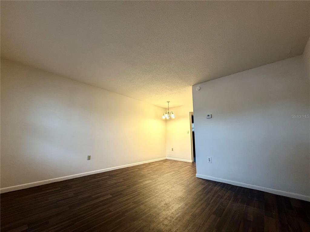 An empty room with dark wood-look flooring, white walls, and a hanging dining light fixture — 710 AVENUE C SW UNIT 4A, WINTER HAVEN, FL
