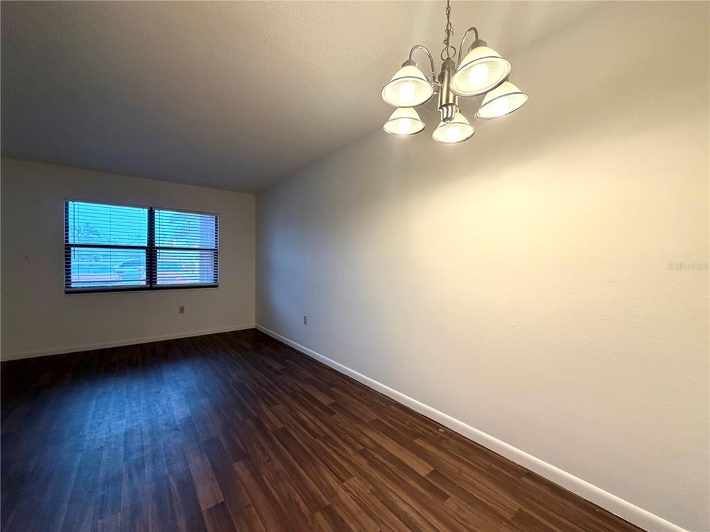 An empty room features dark wood-look flooring, a large window, and a multi-light chandelier — 710 AVENUE C SW UNIT 4A, WINTER HAVEN, FL